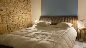 Un lit avec une couette blanche, un mur en pierre, un plafond bleu et deux lampes de chevet.