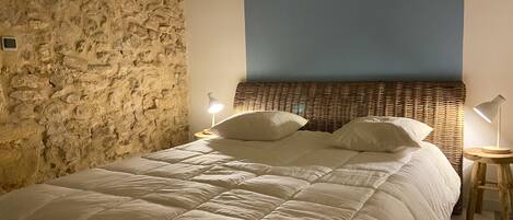 A bed with a white duvet, a stone wall, a blue ceiling, and two bedside lamps.