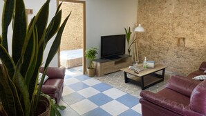 Un salon avec un téléviseur, une table basse, un canapé et une plante en pot.