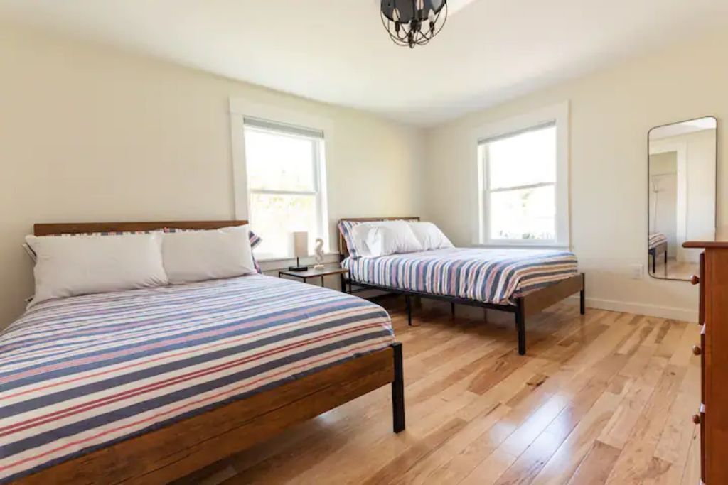Un dormitorio con dos camas, suelo de madera y ventanas amplias.