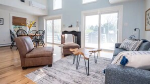 A spacious living room with a brown leather sofa, a grey sofa, and a wooden coffee table. There is a dining area with a table and chairs, and a fireplace.