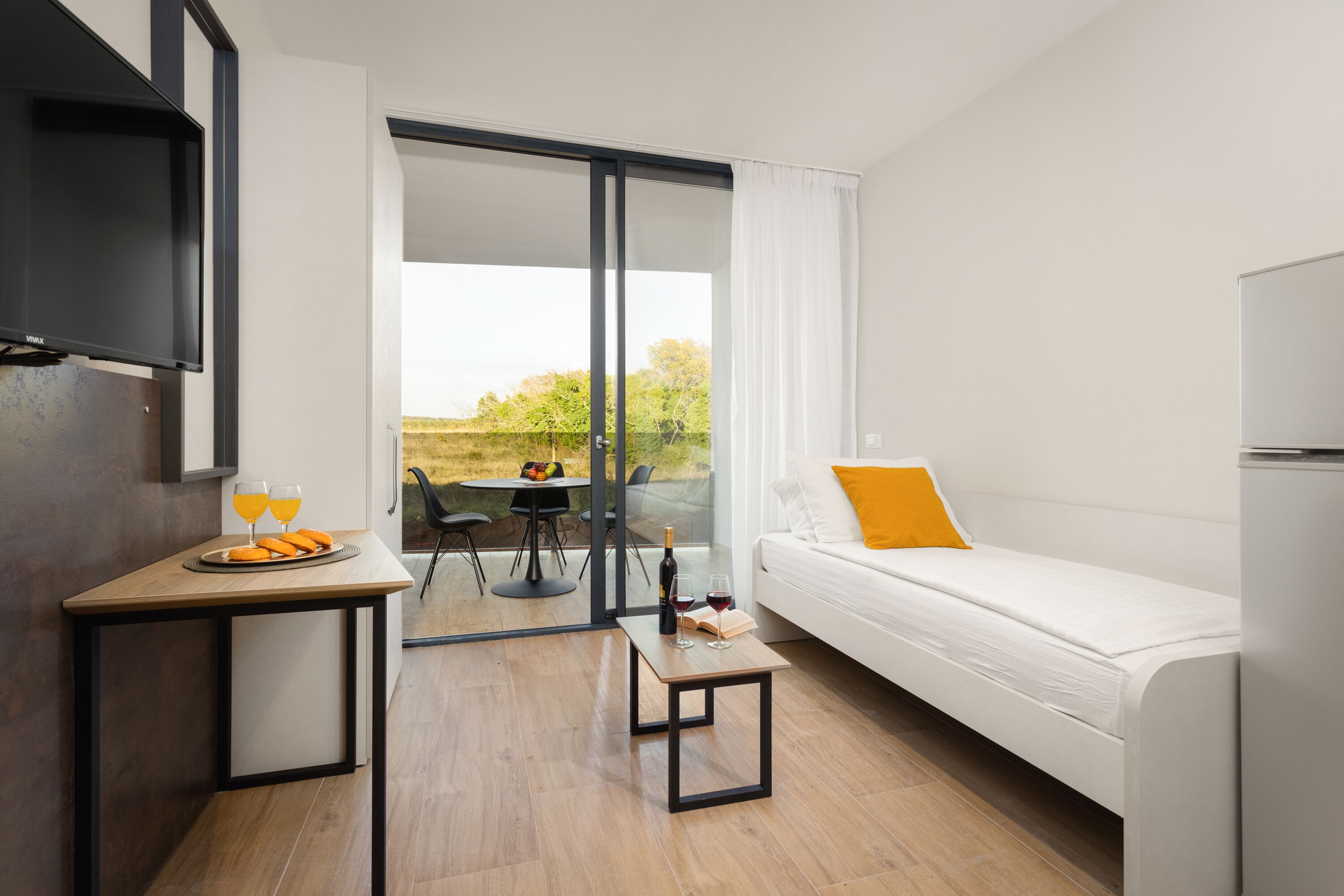 A modern room with a white sofa, a small table with a bottle and glasses, and a TV mounted on the wall.