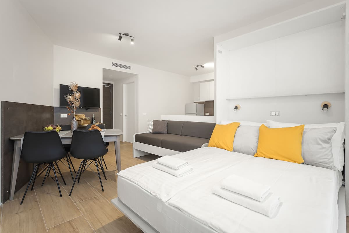 A modern hotel room with a large bed, a sofa, a desk with chairs, and a TV.