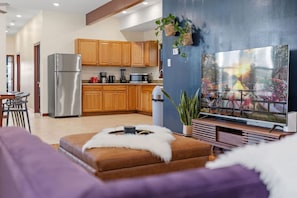 Eine moderne Küche mit Holzschränken, einem Edelstahlkühlschrank und einem Essbereich mit einem violetten Sofa und einem kleinen Tisch.