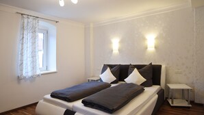 A modern bedroom with a large bed, two bedside tables, a window with curtains, and wall-mounted lighting.