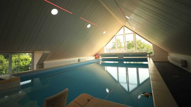 An indoor swimming pool with a sloped ceiling and large windows.