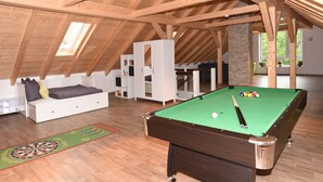 A spacious loft with a pool table, wooden beams, a loft bed, and a view of the outdoors.