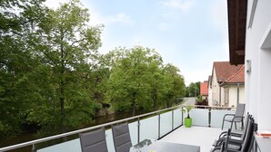 A balcony with a table and chairs, overlooking a river and trees.