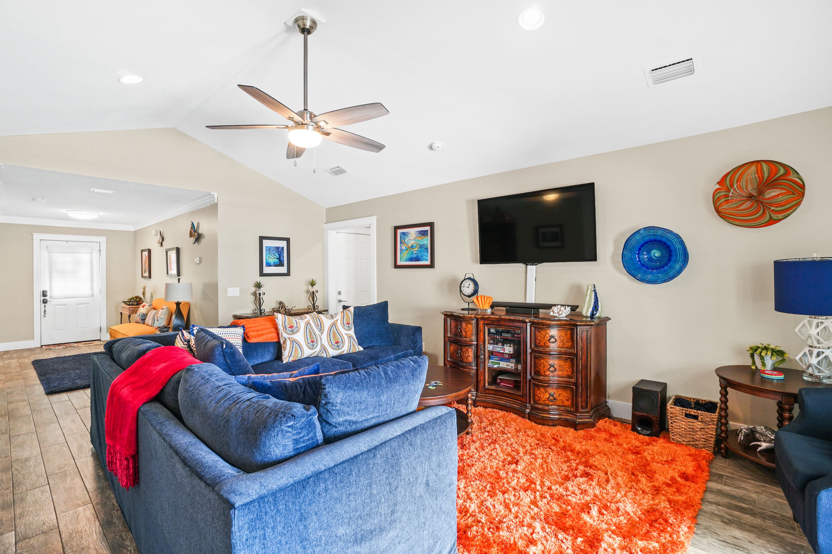 A living room with a blue sofa, orange rug, wooden cabinet, and a flat-screen TV.