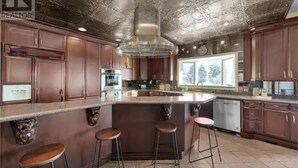 A kitchen with dark wood cabinets, a large island with stools, and a decorative ceiling. - Luxury Villa next to golf course (LaSalle)