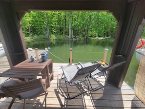 A wooden deck with a table and chairs, overlooking a calm body of water and dense greenery.