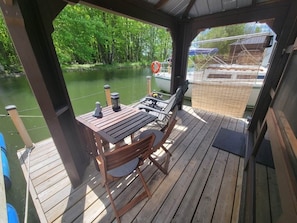 Una terraza de madera con una mesa y sillas, con vista a un río tranquilo y barcos.