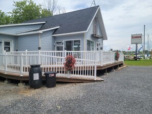 A building with a covered deck, a white fence, and a signboard. - Aloberge 2 (Lacolle)