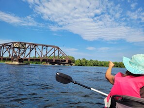 Una persona en kayak en un río, con un puente al fondo.