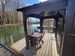 A wooden deck with a table and chairs, overlooking a body of water. - Aloberge 2 (Lacolle)