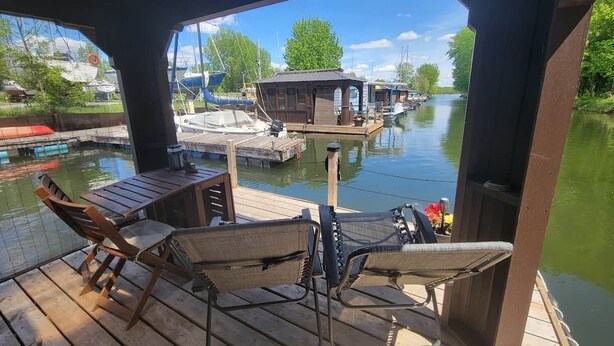 Une terrasse extérieure couverte, aménagée avec des meubles en bois et offrant une vue sur une rivière où naviguent des bateaux.
