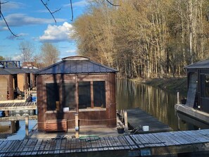 Una cabaña de madera con un muelle que se adentra en un río tranquilo, rodeada de árboles.