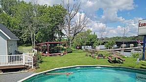Une piscine avec une terrasse en bois, des tables de pique-nique et une aire de jeux couverte.