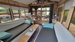 Une cabine avec un intérieur en bois, un canapé, une table avec un menu et de grandes fenêtres donnant sur une zone abritant des quais.