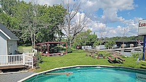 A swimming pool with a wooden deck, picnic tables, and a covered play structure. - Aloberge 5 (Lacolle)