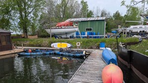 A dock with kayaks, a boat, and a green building. - Aloberge 5 (Lacolle)