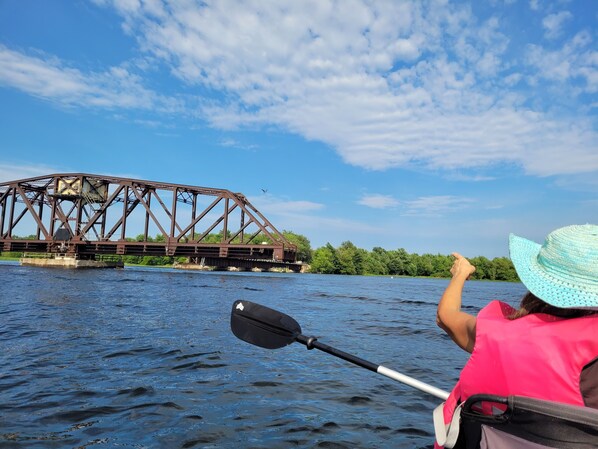 Une personne pratiquant le kayak, avec un pont métallique en arrière-plan.