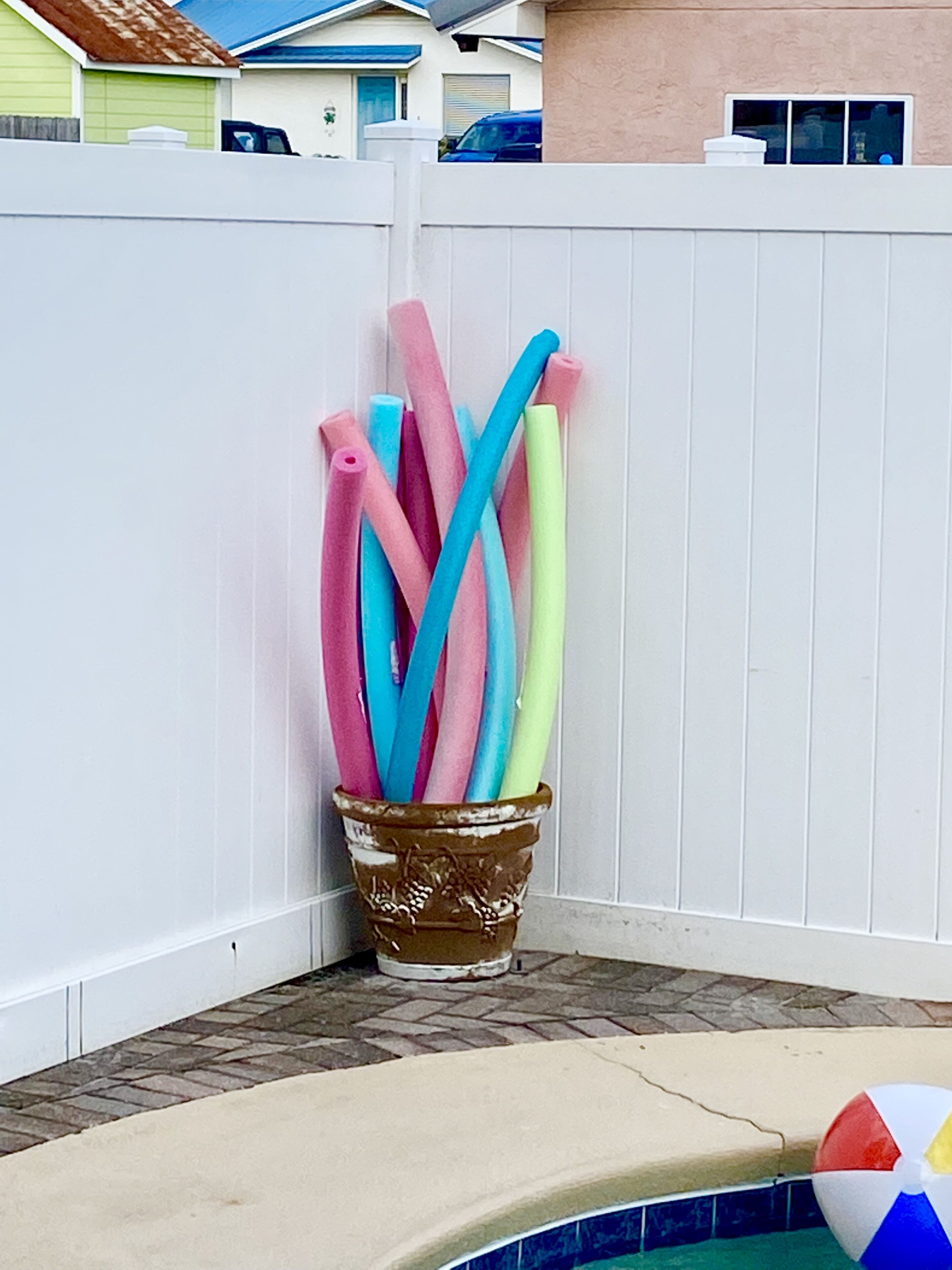 A white fence with a planter containing colorful pool noodles.