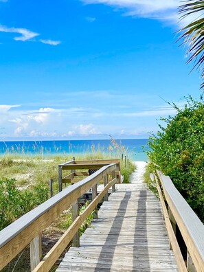 A wooden boardwalk leading to a beach with clear skies and ocean views.