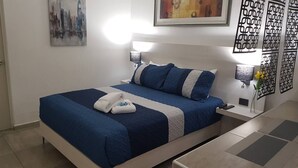 Ein ordentlich bezogenes Bett mit blauer und weißer Bettwäsche, zwei Nachttische mit Lampen, ein Stadtbild in einem Bilderrahmen und ein dekoratives Wandpaneel.