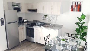 Une cuisine compacte équipée d’un réfrigérateur, d’une cuisinière, d’un four à micro-ondes et d’un évier. On y trouve une table à manger avec des chaises et une plante en pot.