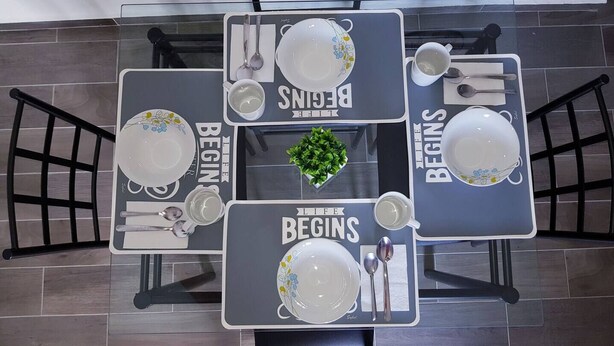 Un espace repas comprenant quatre tables, chacune agrémentée d’un set de table sur lequel est inscrit « LA VIE COMMENCE » et d’une plante en pot placée au centre.