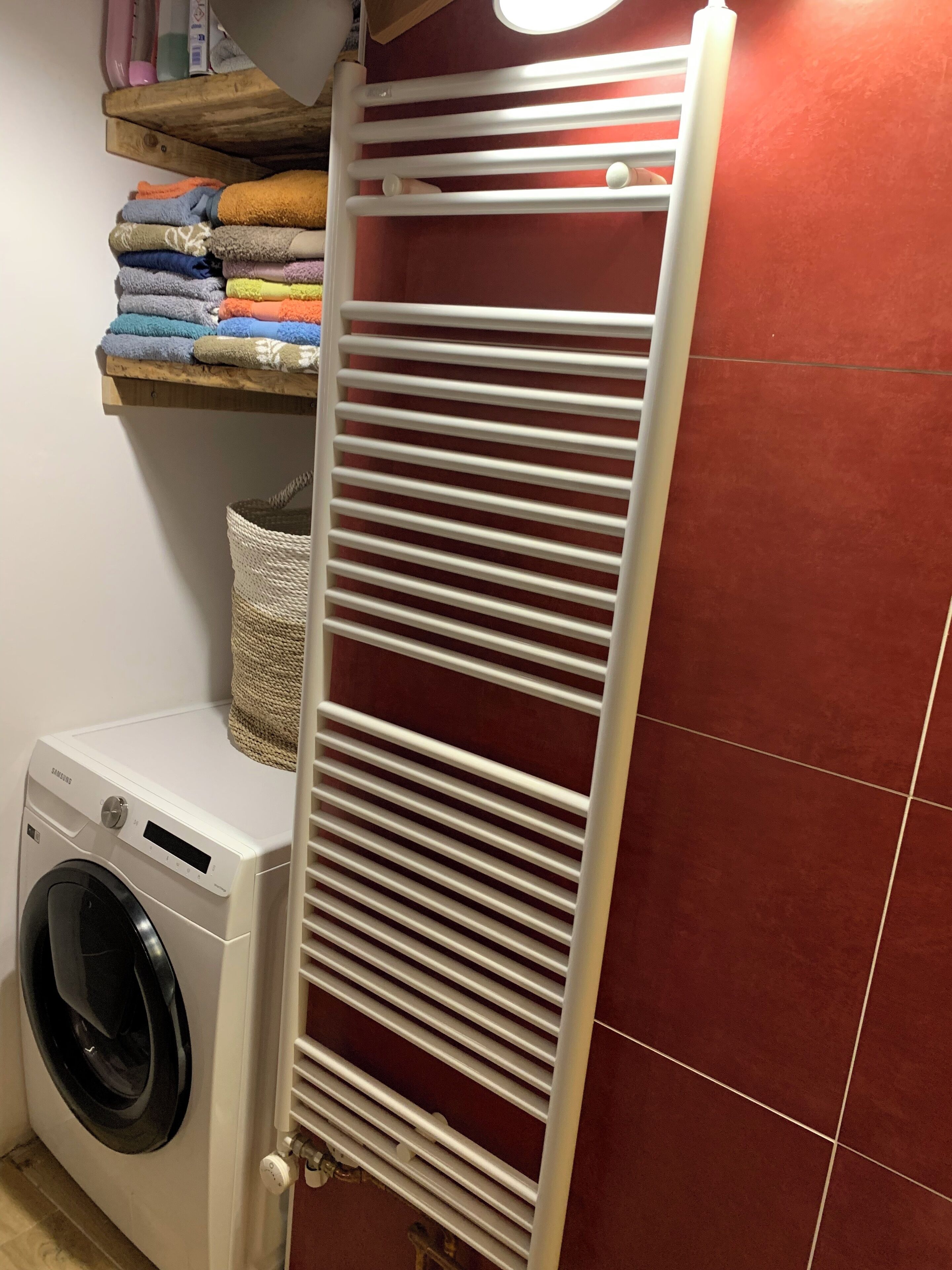 Un espace dédié à la lessive, comprenant un lave-linge blanc, un étendoir et une étagère avec des serviettes pliées.