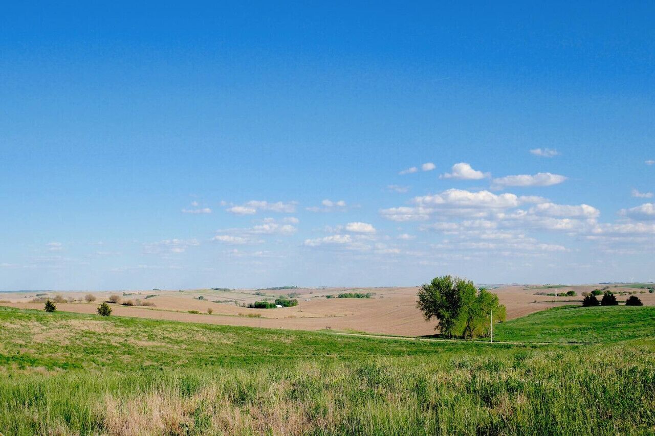 A rural landscape with rolling hills, a clear sky, and scattered clouds.