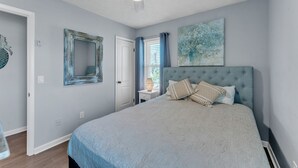 Un dormitorio con una cama grande, un ventilador de techo, una ventana con cortinas y un espejo montado en la pared.