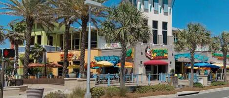 Une vue de rue avec un bâtiment abritant un restaurant, reconnaissable à ses parasols colorés et à une enseigne indiquant « PIZZA ».