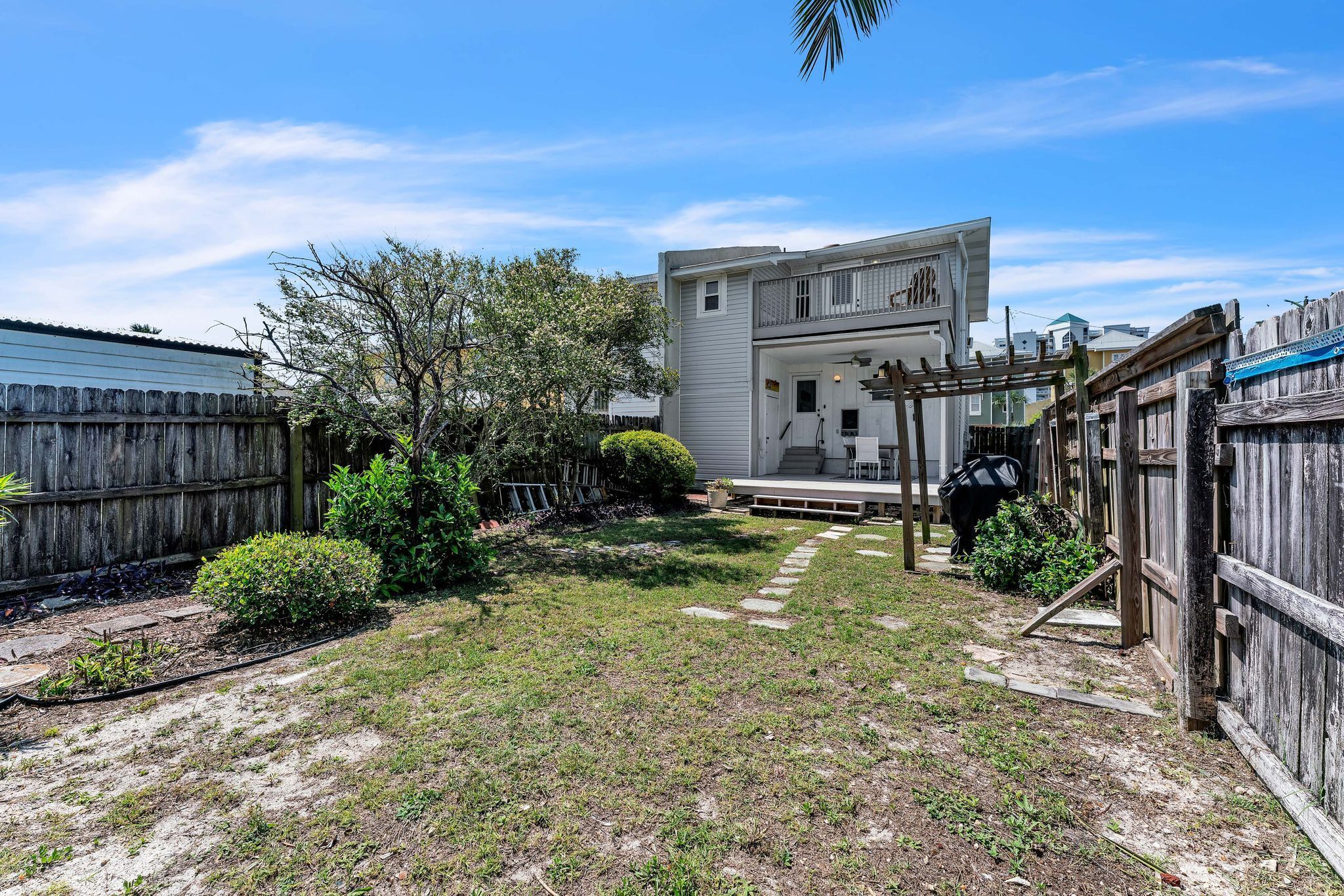 A residential backyard with a wooden fence, a small garden, and a two-story house with a porch.