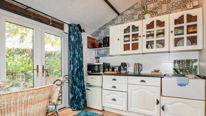 A kitchen with white cabinets, a microwave, a coffee maker, and a wicker chair. - Carminow Barn (Bodmin)