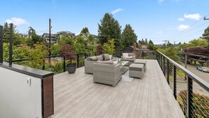 A rooftop deck with outdoor furniture, a view of houses and trees, and a street with cars. - Guesthouse in Phinney Ridge with Rooftop Deck (Seattle)