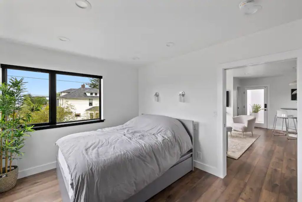 A modern bedroom with a large window, a bed, and a view of a house outside.