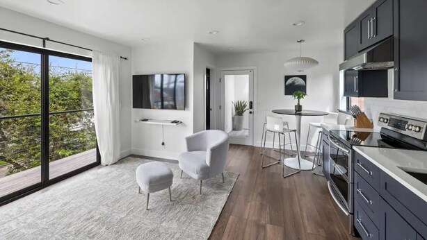A modern kitchen with dark cabinets, a large stove, and a dining area with white chairs and a round table. - Guesthouse in Phinney Ridge with Rooftop Deck (Seattle)