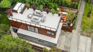 A modern two-story building with a flat roof, large windows, and a balcony with outdoor seating. - Guesthouse in Phinney Ridge with Rooftop Deck (Seattle)
