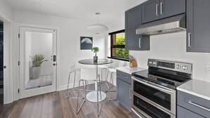 A modern kitchen with grey cabinets, a stainless steel oven, and a round dining table with chairs. - Guesthouse in Phinney Ridge with Rooftop Deck (Seattle)