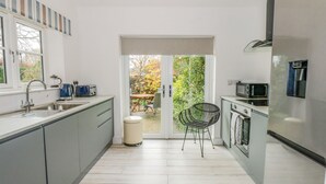 A modern kitchen with grey cabinets, a stainless steel sink, a microwave, and a refrigerator. There is a window with a view of a garden.