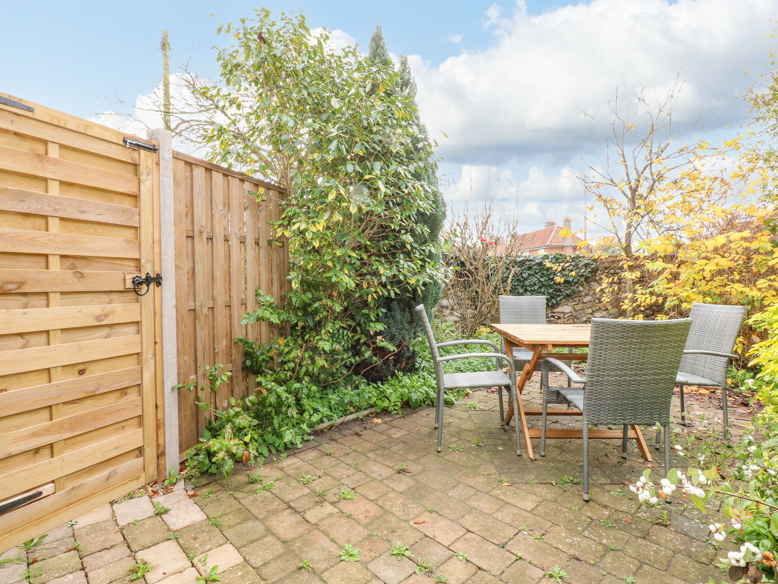 Eine Terrasse mit Holztisch und -stühlen, umgeben von einem Holzzaun und verschiedenen Pflanzen.