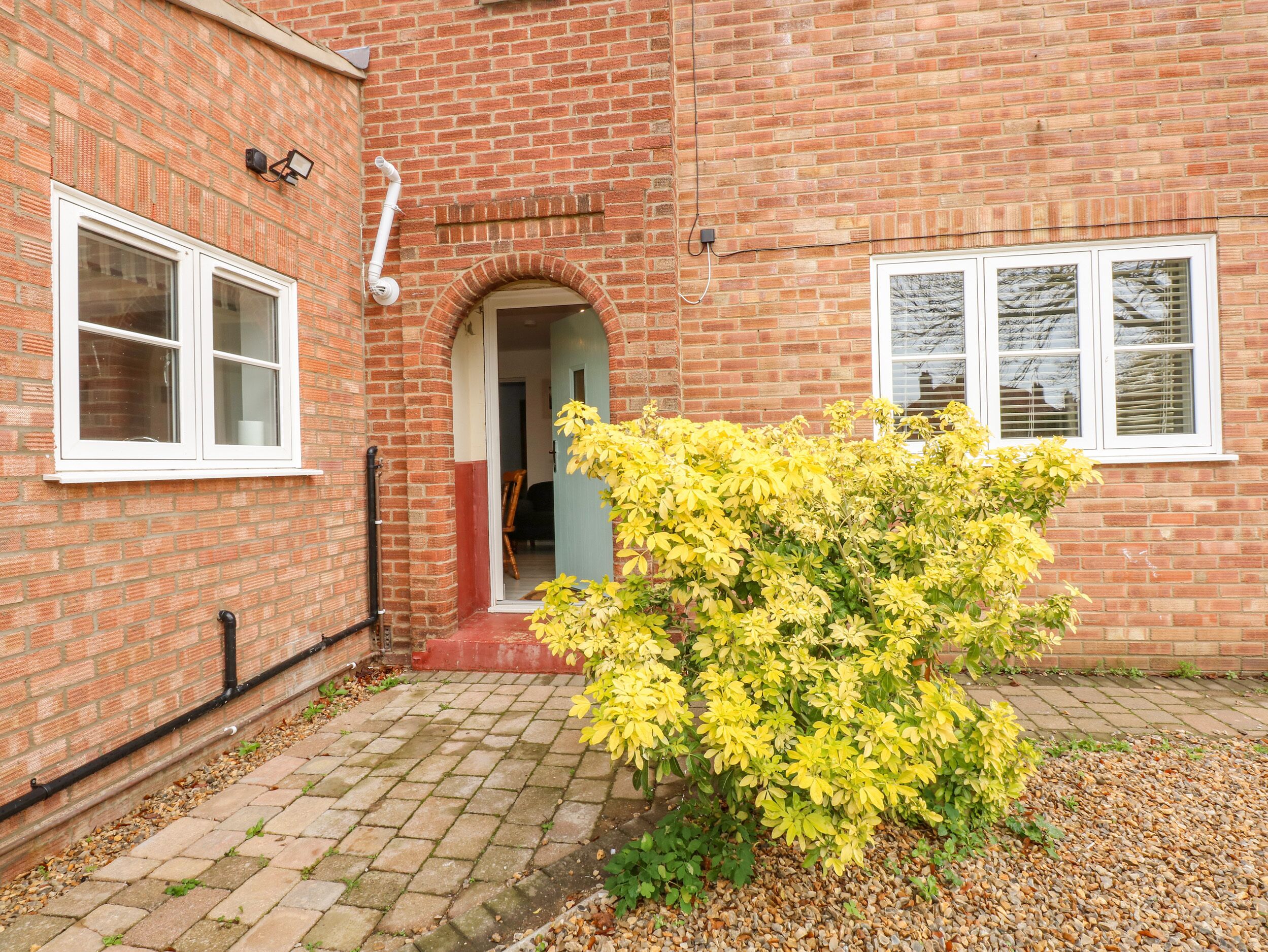 A brick building with a red door, white windows, and a yellow flowering bush in the foreground.