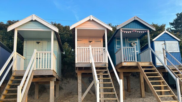 Three beach huts with wooden staircases leading to the entrance.