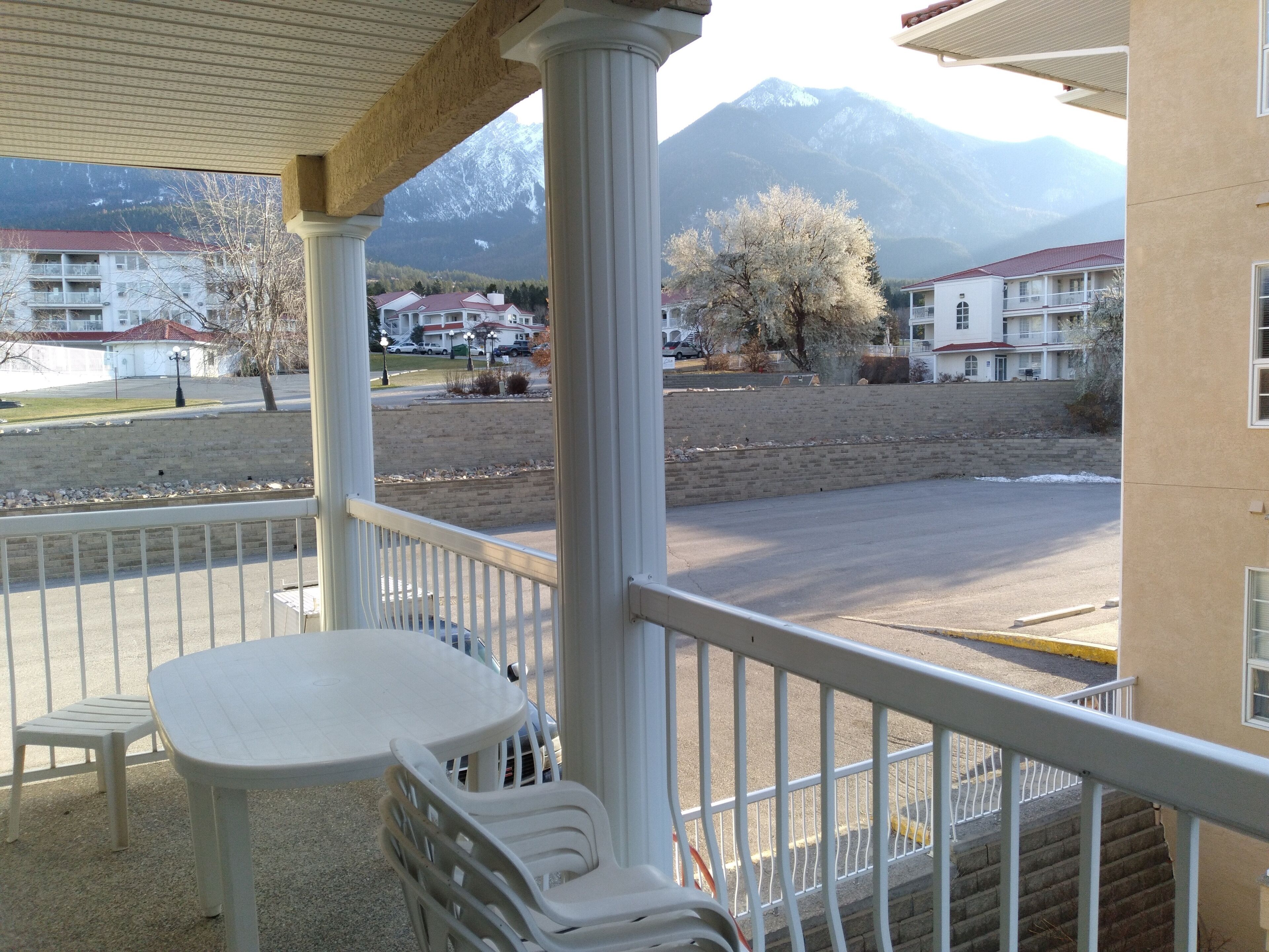 A balcony with a view of a mountain, a parking lot, and buildings in the background.