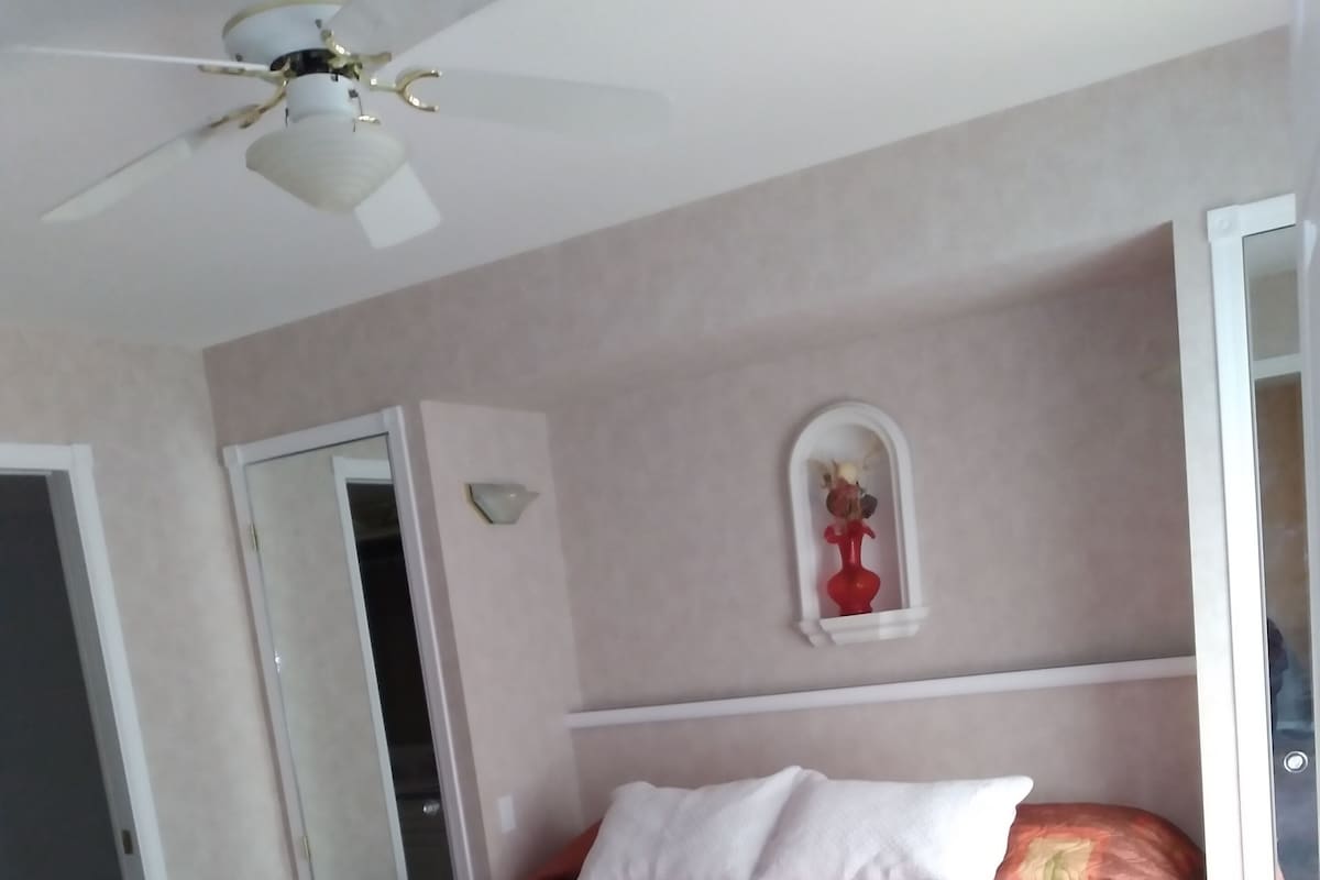 Ein Schlafzimmer mit Bett, Deckenventilator, Kommode und Spiegel.