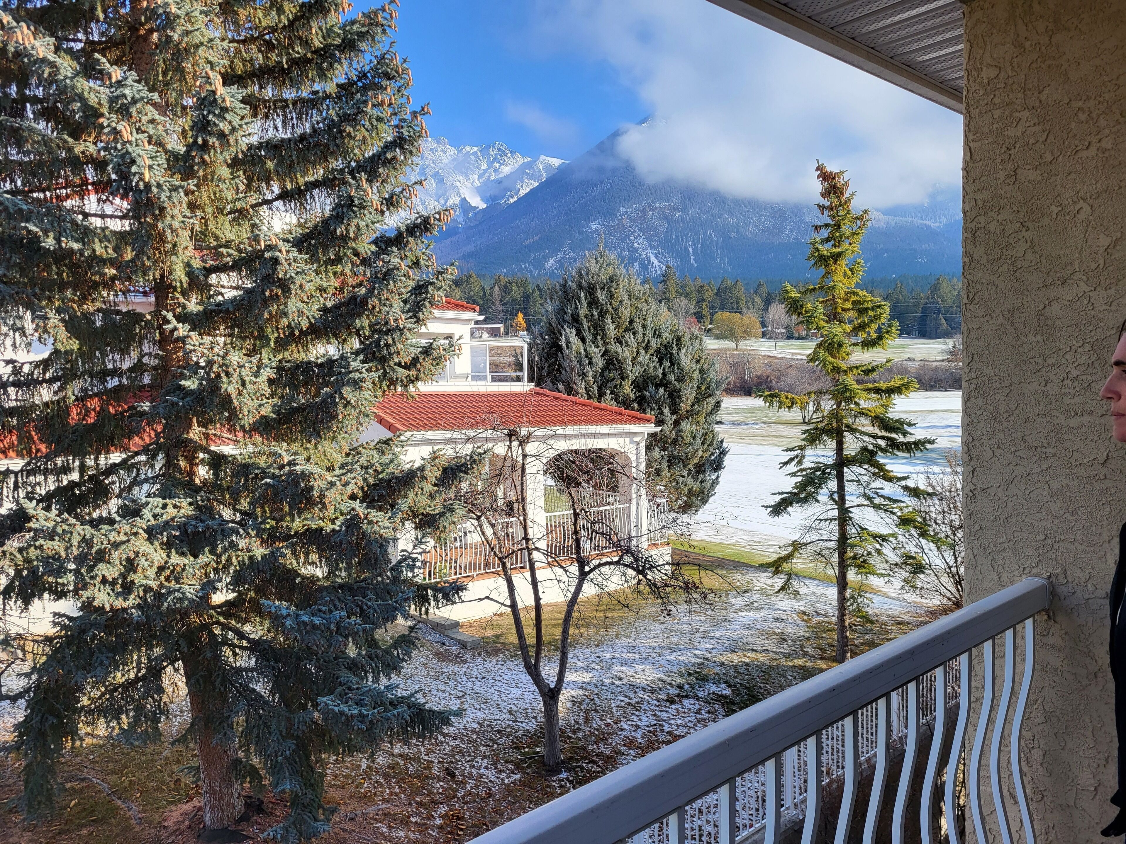 A balcony with a view of a snow-covered landscape, a building with a red roof, and a mountain in the background.