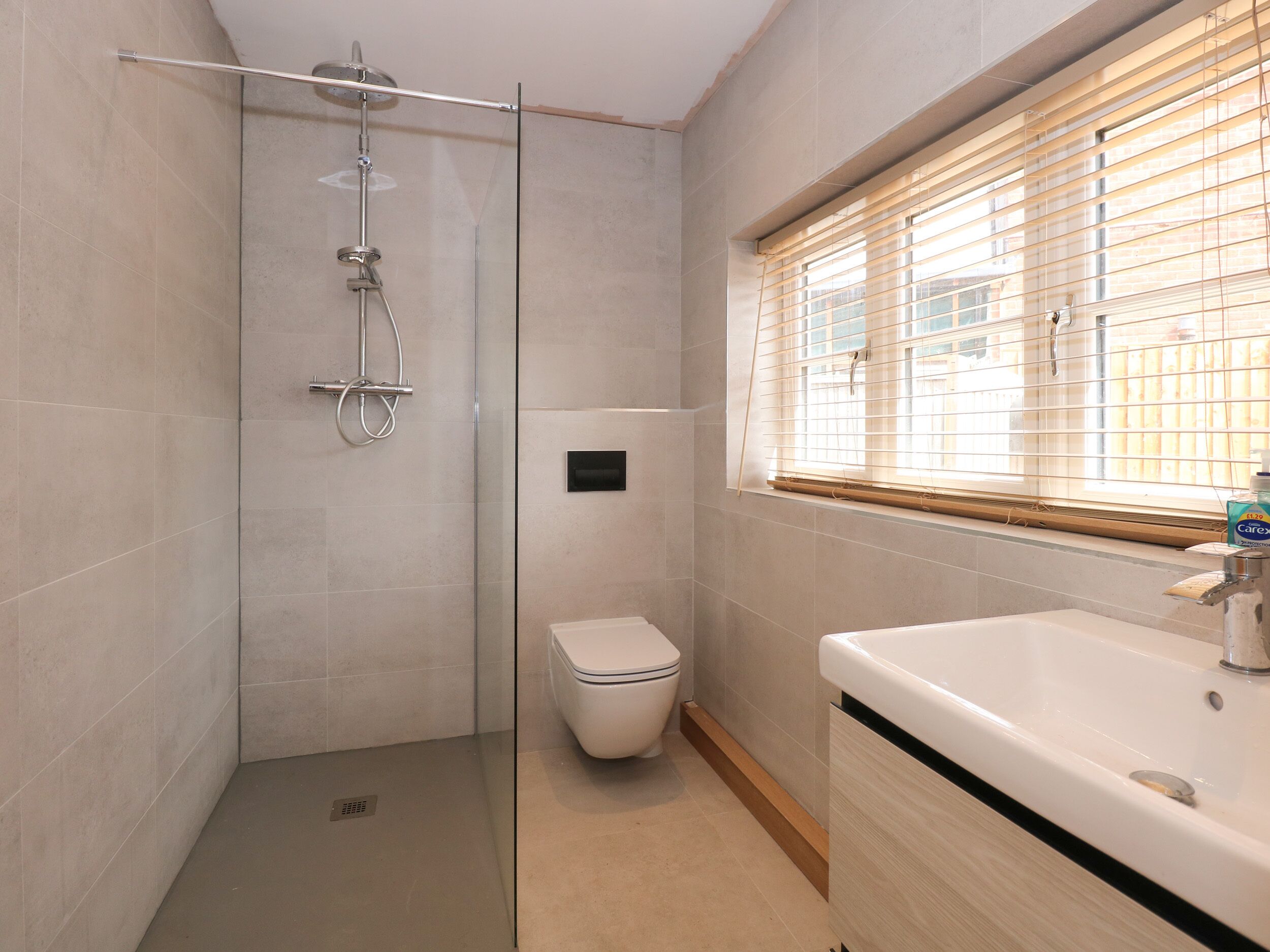 Ein modernes Badezimmer mit einer gläsernen Duschkabine, einer Toilette und einem Waschbecken mit Fenster darüber.